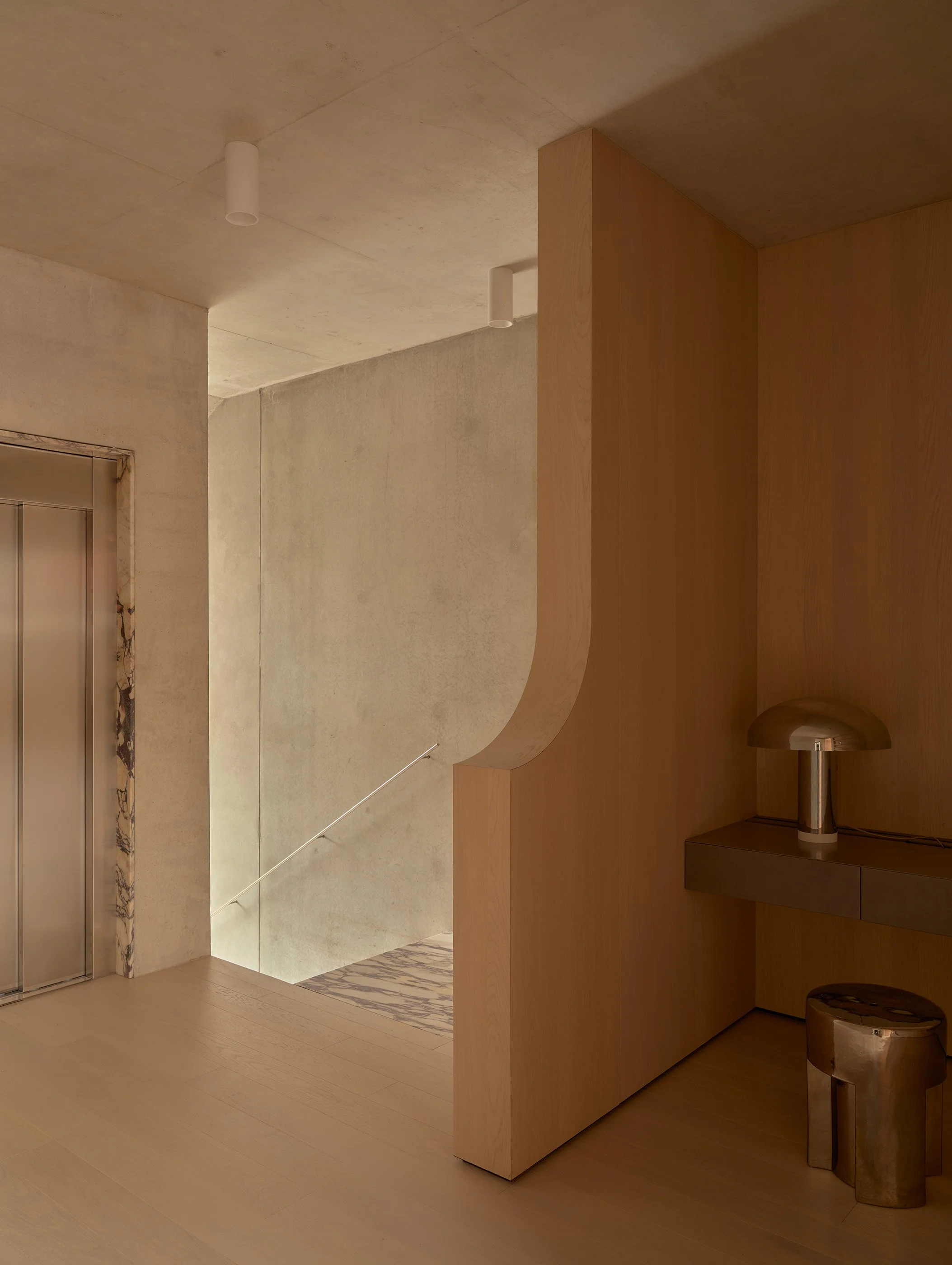 Interior view of a modern building with an elevator, wooden wall, minimalist lamps, and a polished metal trash bin.
