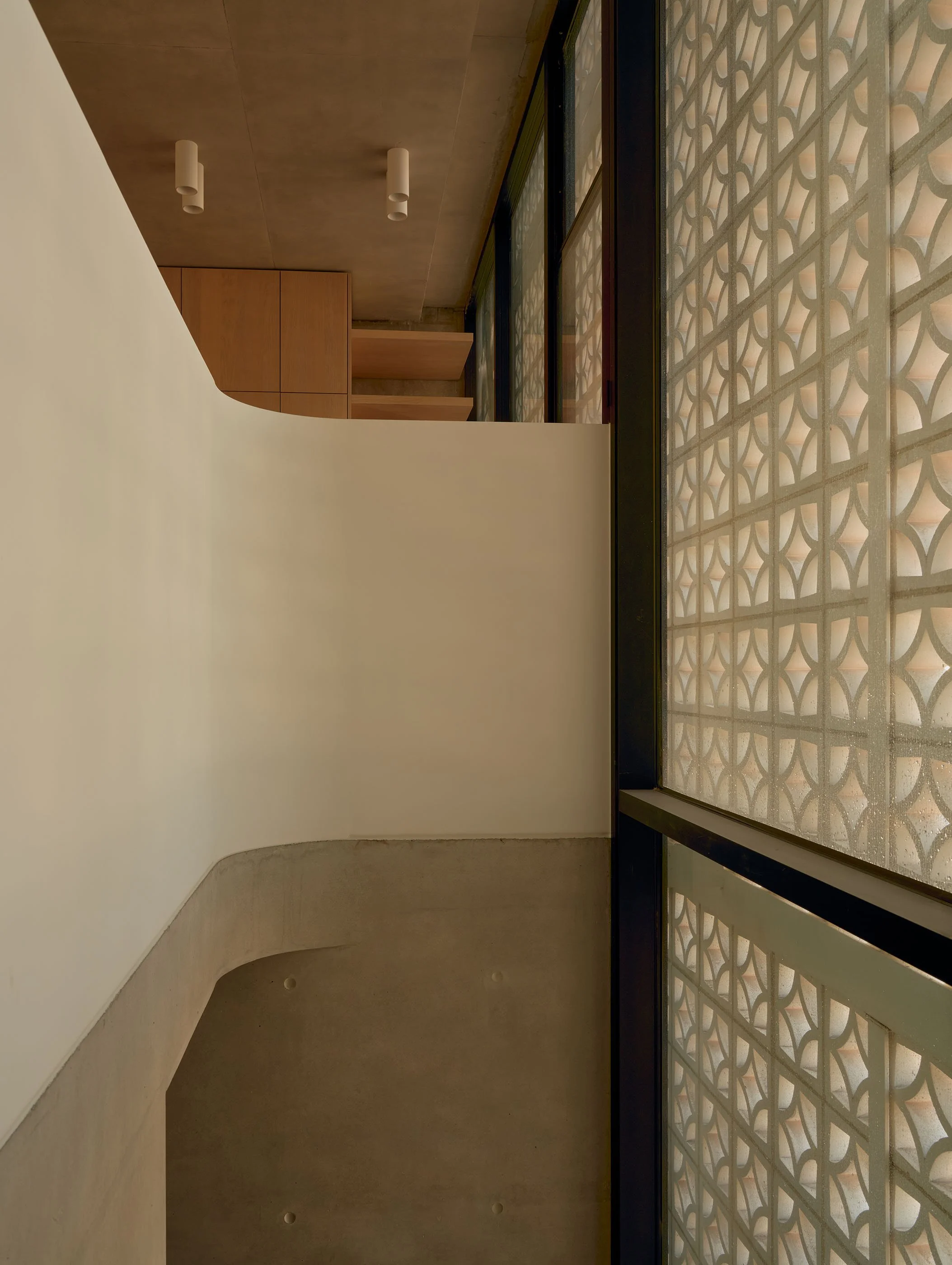 Interior view of a modern building with a curved concrete bench, wood cabinets, large windows with decorative frosted glass, and cylindrical ceiling lights.
