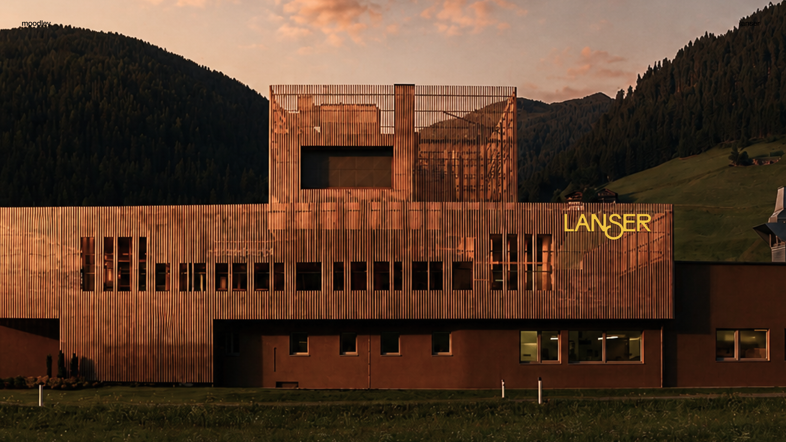 Moderne Holzfassade eines Gebäudes, umgeben von grüner Landschaft mit Hügeln und Bäumen bei Sonnenuntergang, mit dem Schriftzug 'LÄNSER' auf der rechten Seite.