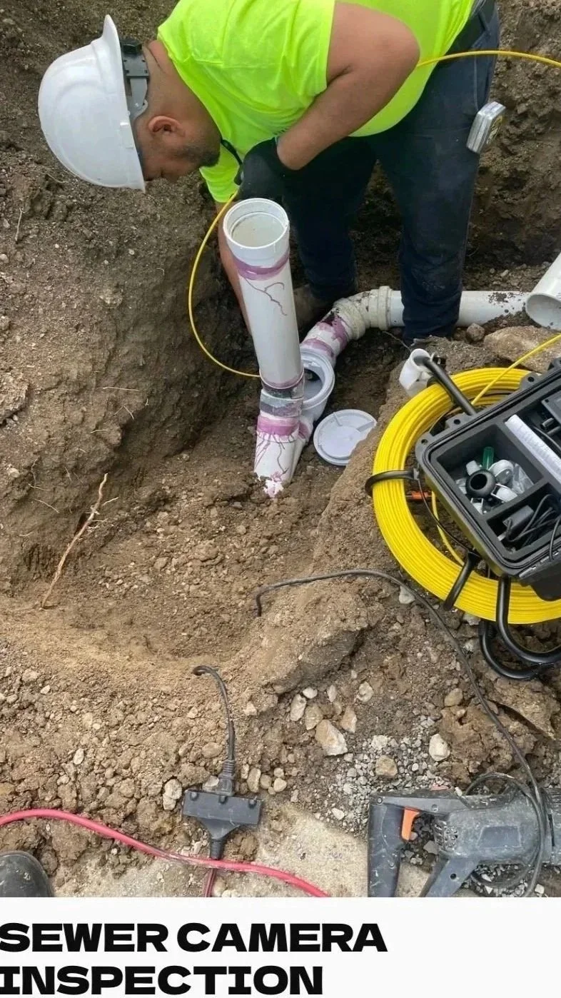 A worker inspecting a sewer camera pipe in an excavation site with tools and equipment nearby.