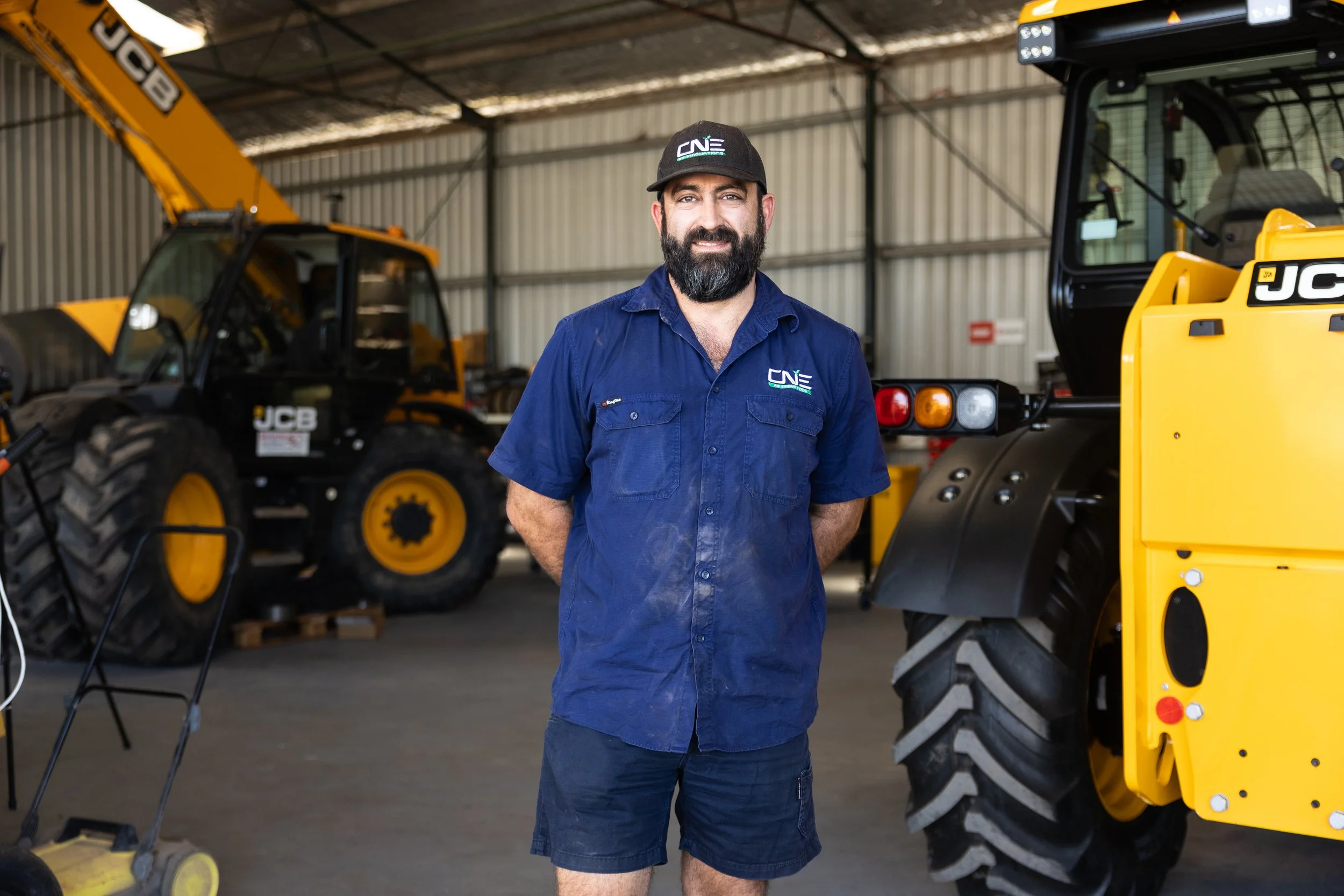 CNE Ag Innovations technician in the workshop between JCB machines