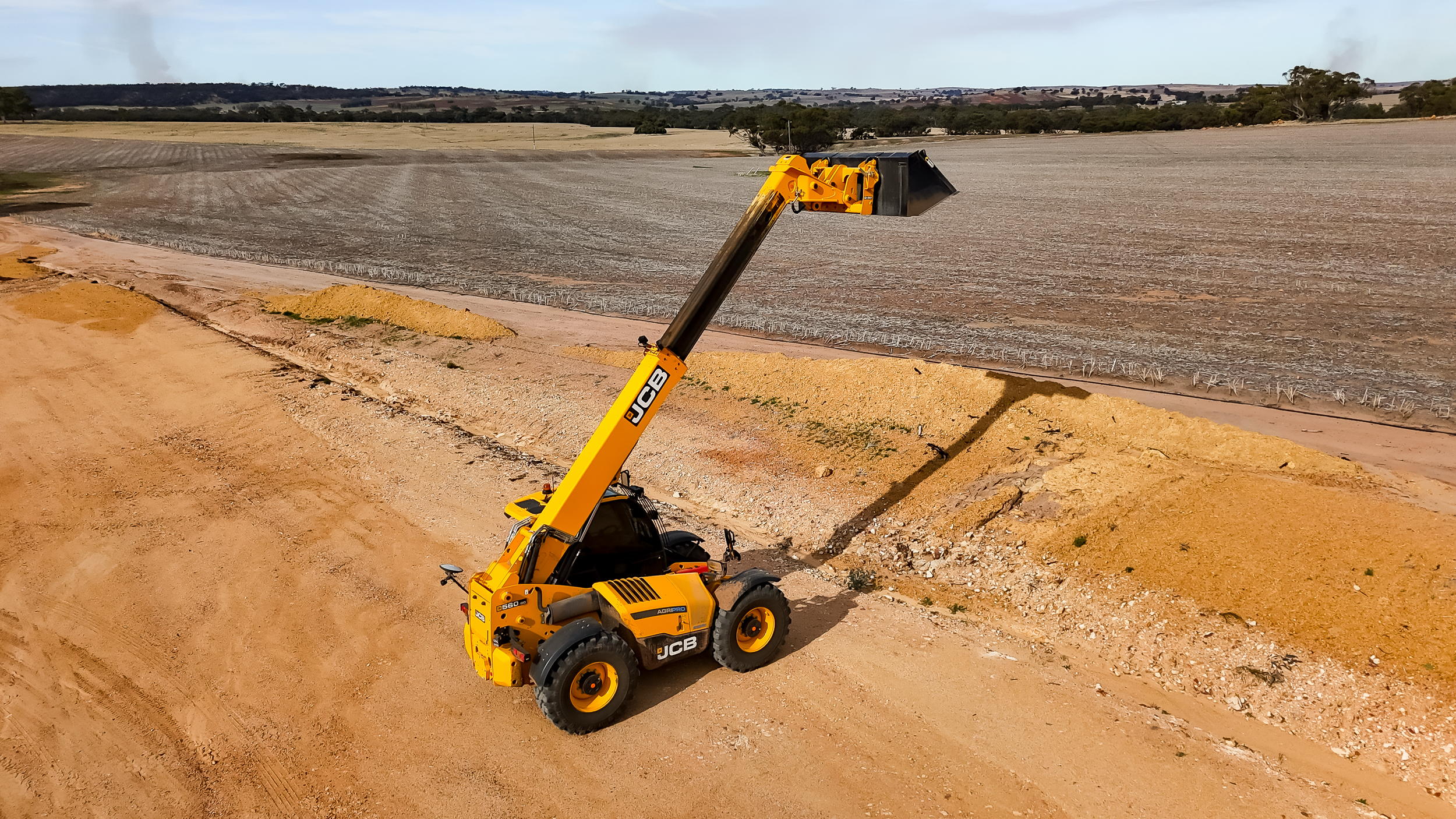 Aerial view of a JCB telehandler with bucket raised on farmland