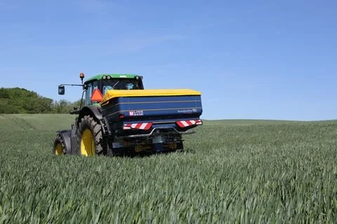 Bogballe M35W fertiliser spreader on a tractor in a green cereal crop