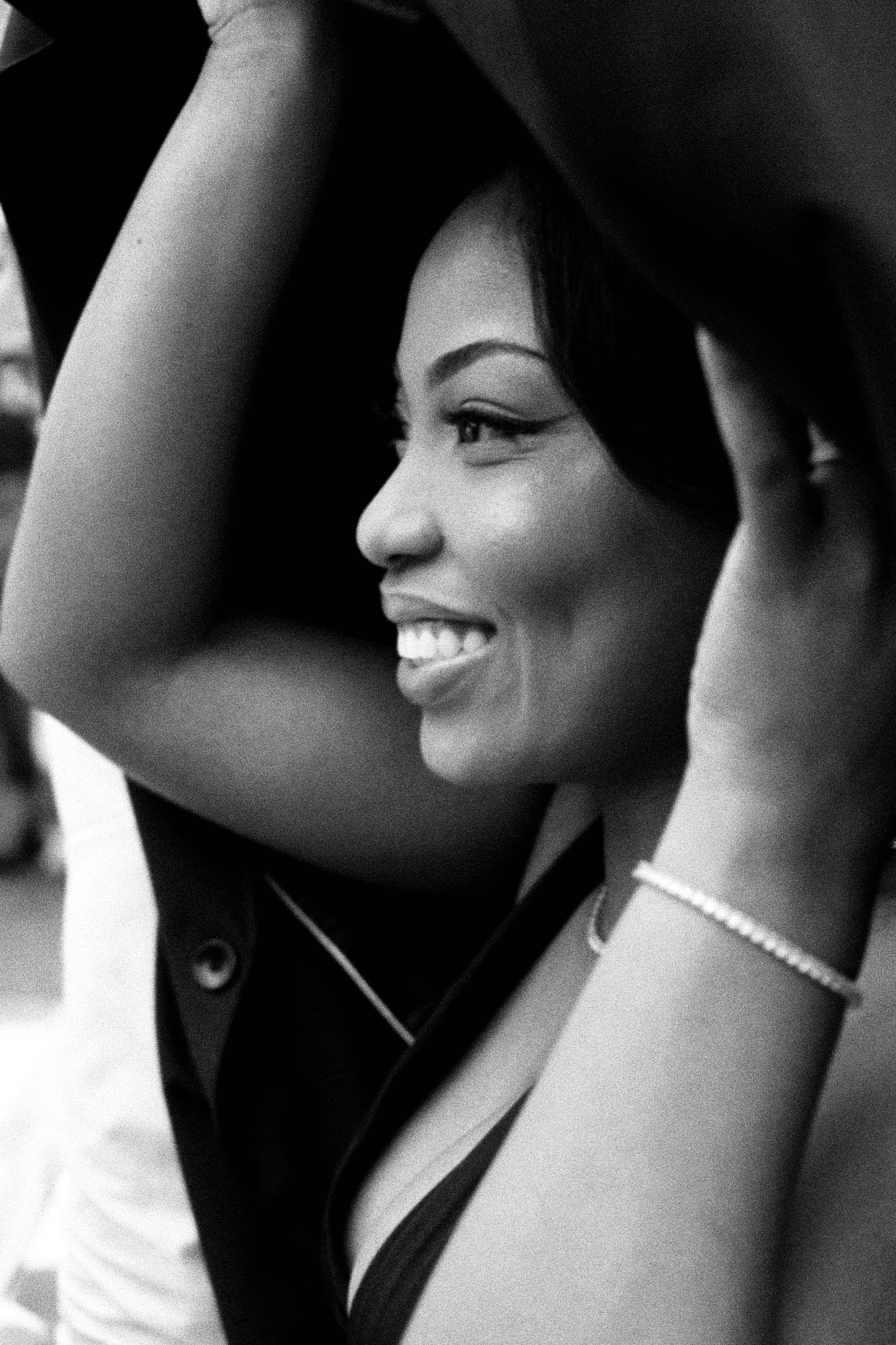 Black and white close-up photo of a smiling woman with dark hair wearing a sleeveless top and a pearl necklace.