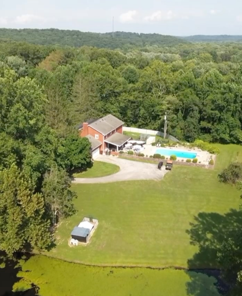 Aerial view of a house with a backyard pool, surrounded by trees and greenery.