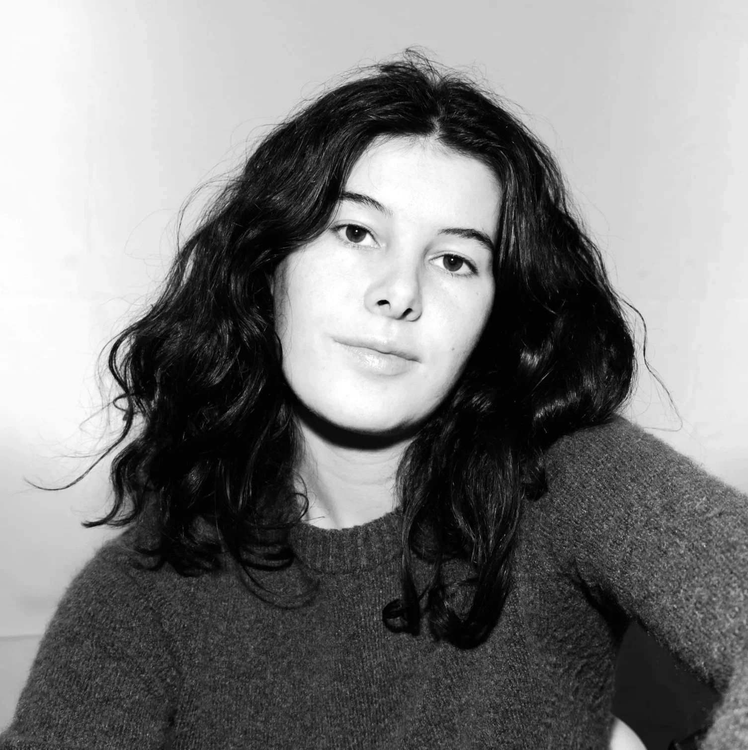 Portrait noir et blanc d'une jeune femme avec des cheveux bouclés, portant un pull en laine.