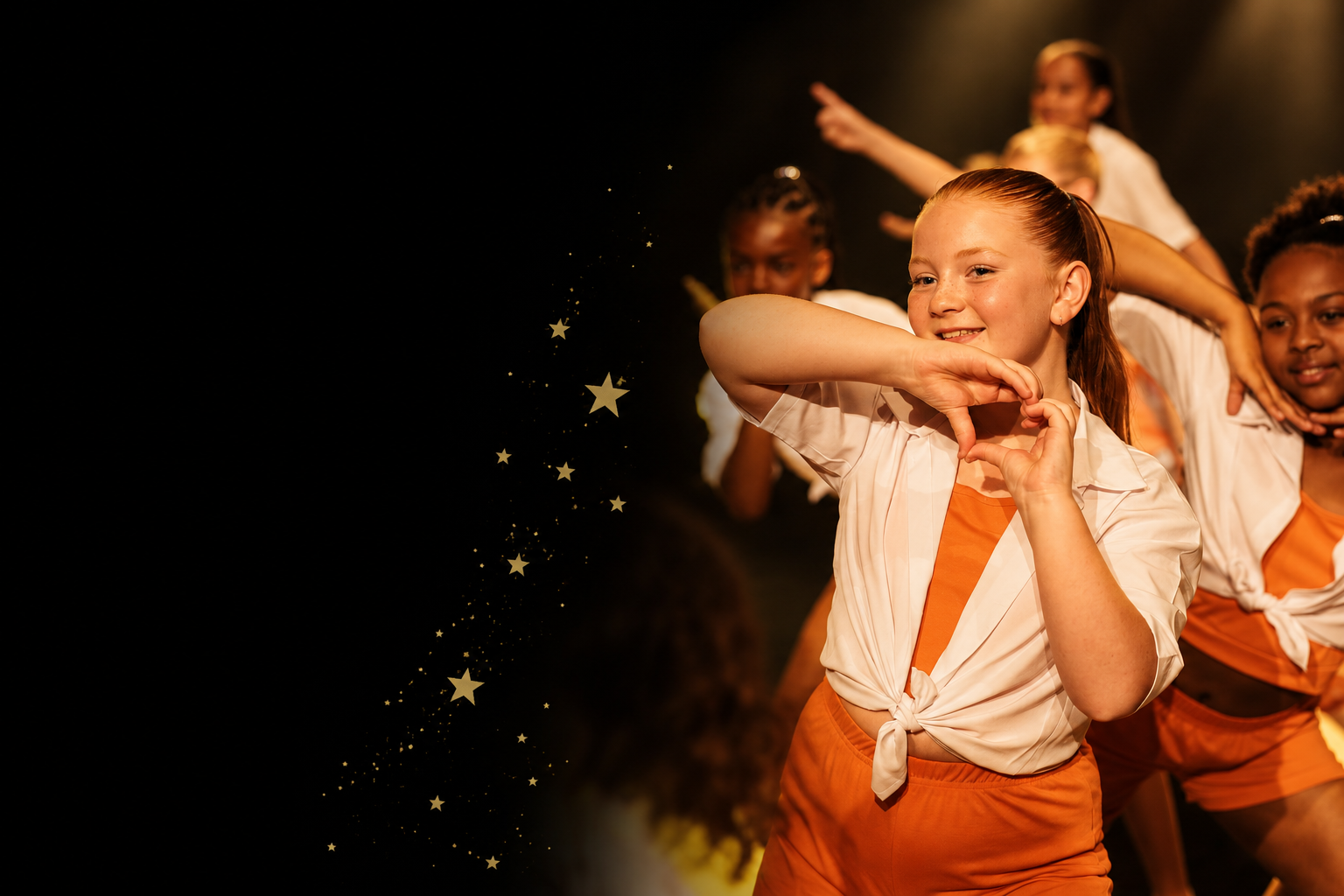 Young girls dressed in orange and white outfits are performing a dance on stage with a spotlight, with some smiling and showing hand gestures, and a trail of stars on the left side of the image.