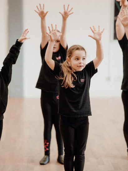 Young student raising her hands during a Stroud Theatre Arts performing arts class.