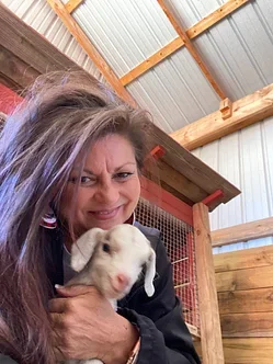 Woman holding a small white puppy inside a wooden structure.