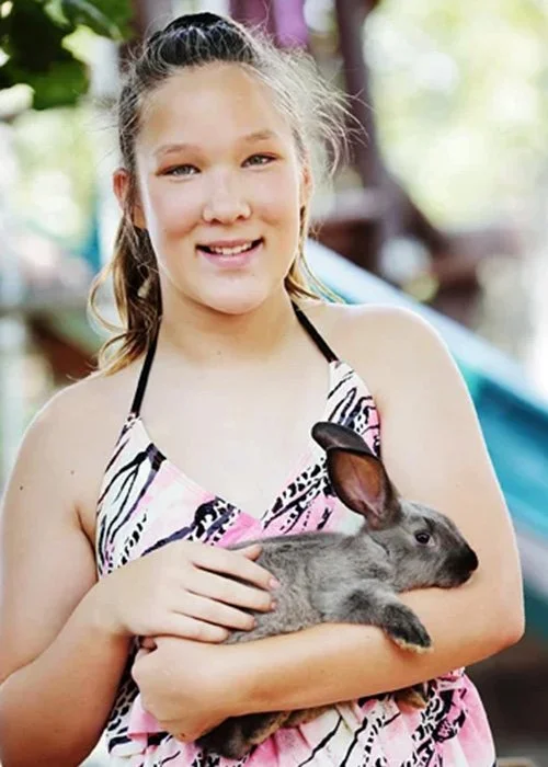 A young girl smiling and holding a gray rabbit outdoors.