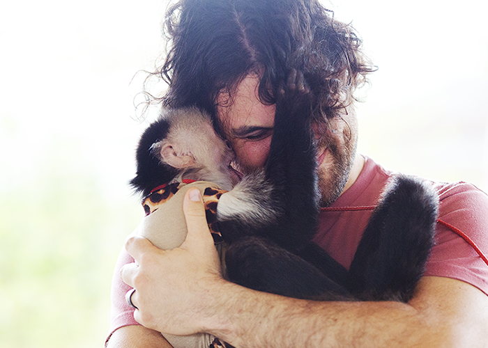 A person with curly hair and a beard is hugging a black and white dog, with the dog’s face pressed against the person’s face.