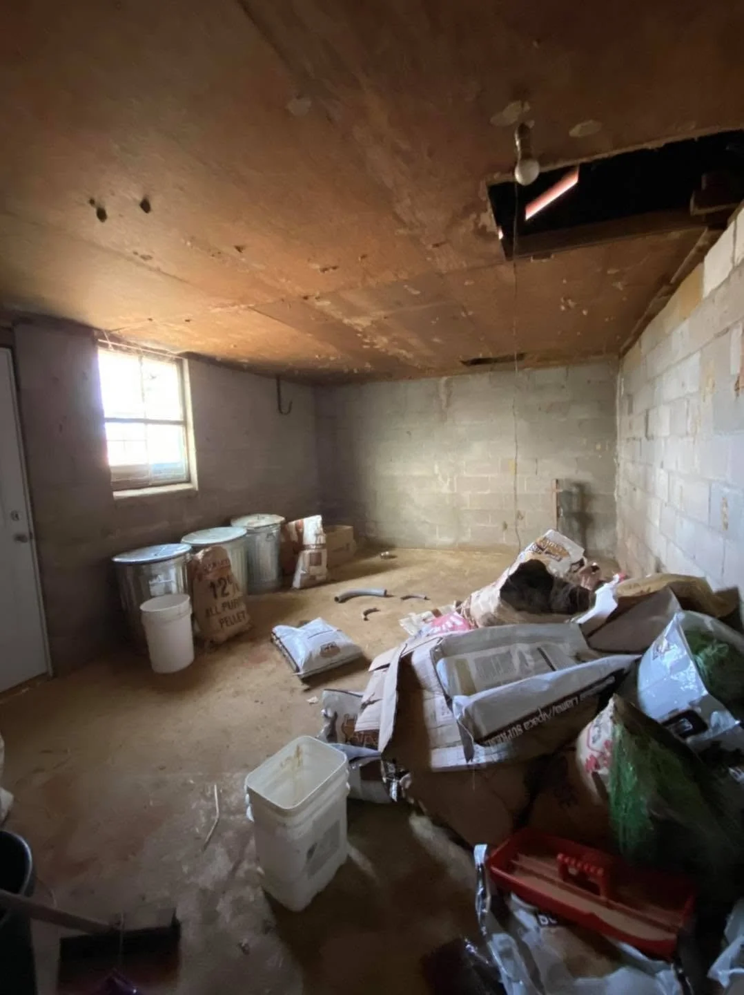 unfinished basement with cinder block walls, a small window, and construction debris including bags of insulation or drywall, buckets, and miscellaneous supplies scattered on the floor.