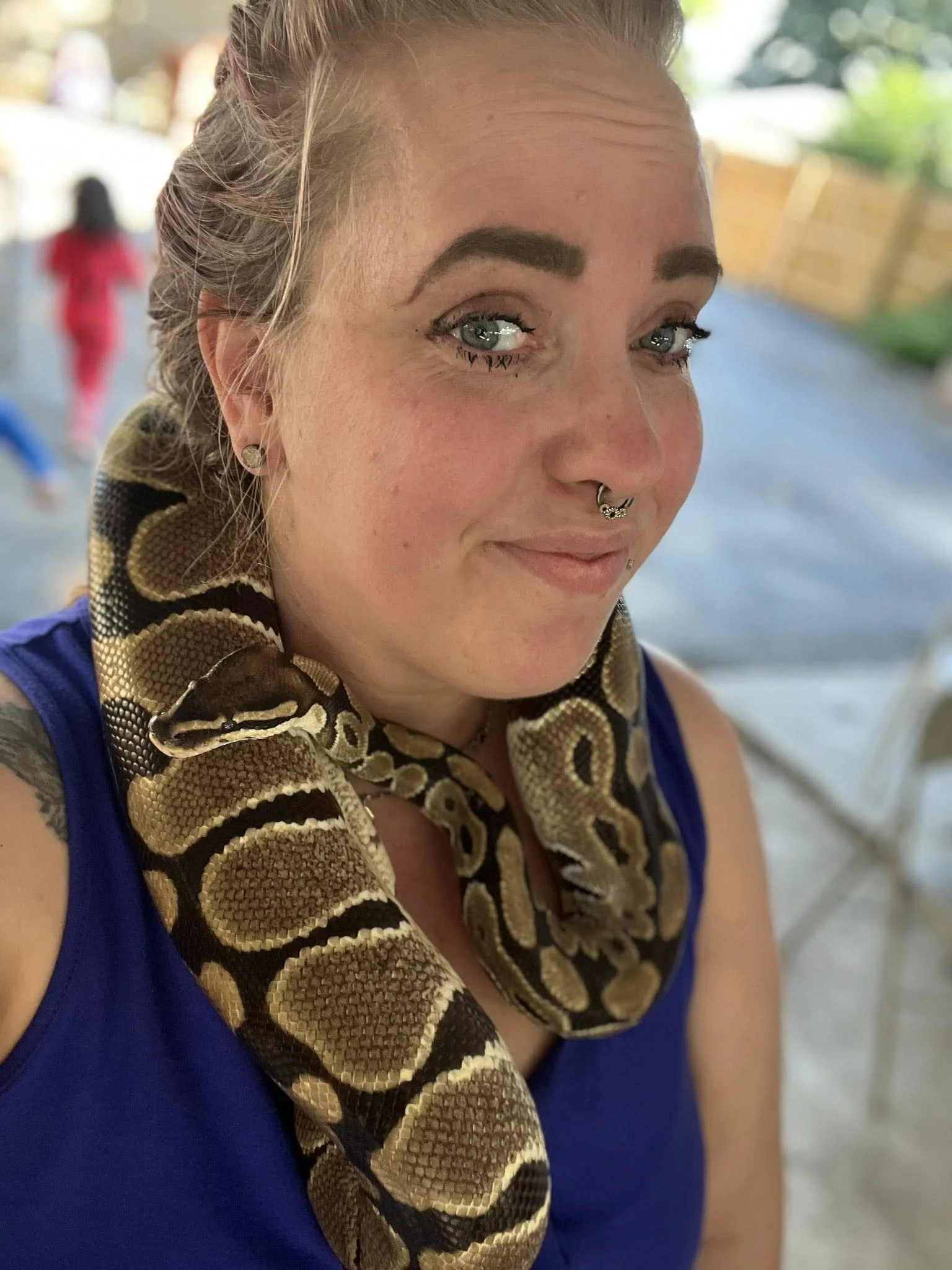 Close-up of a woman with a snake on her shoulder, outdoors.
