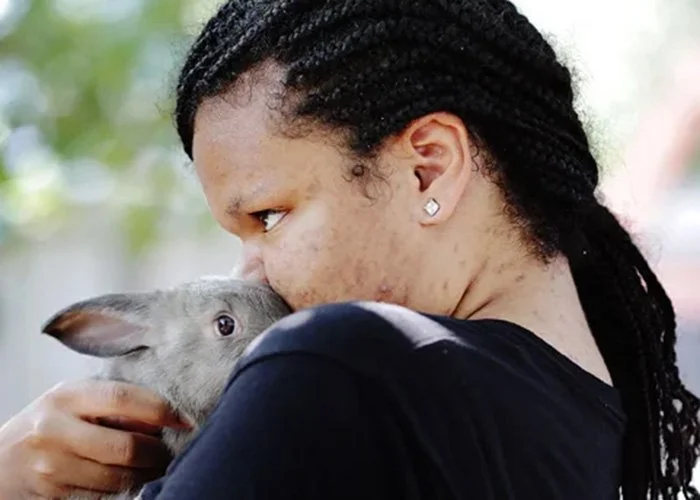 Woman holding a gray rabbit close to her face outdoors
