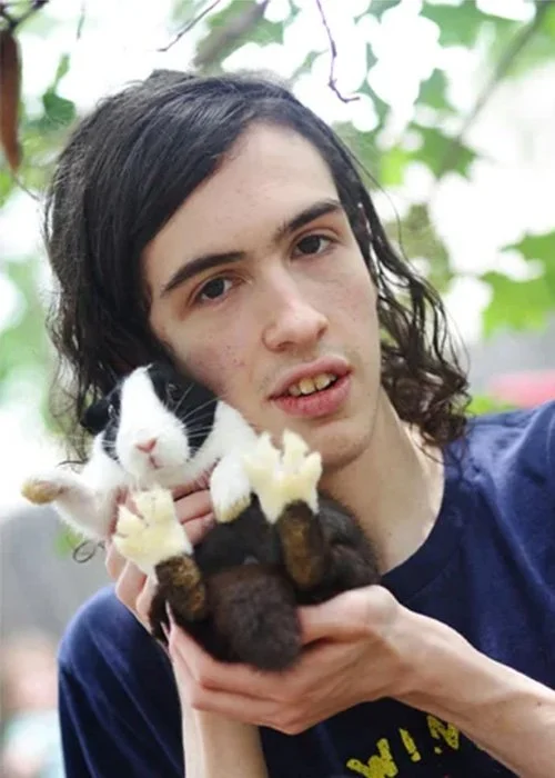 Young man holding a black and white rabbit with a person with long hair in the background.