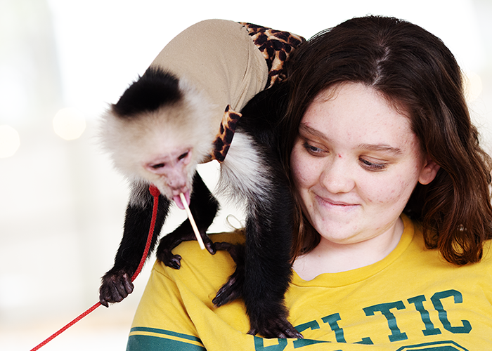 Young girl with shoulder-length brown hair and freckles holding a black and white monkey wearing a beige outfit with leopard print accents
