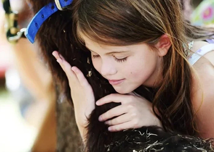 A young girl hugging a black rabbit, with her eyes closed and a gentle smile.
