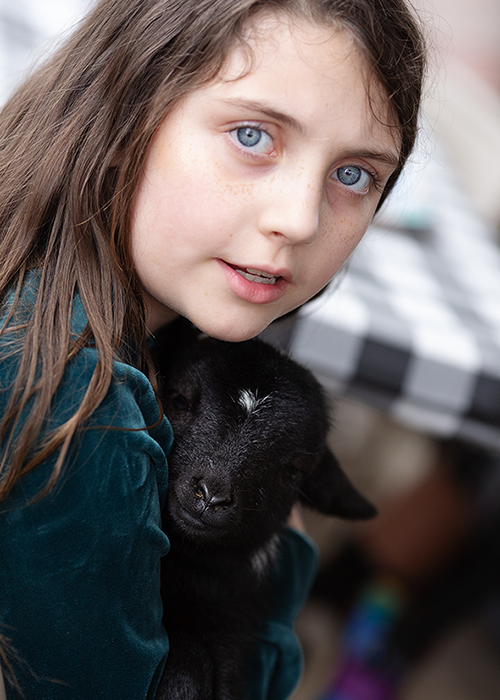 A girl with blue eyes holding a black puppy.