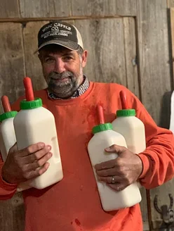 Man holding four squeeze bottles, two with red nozzles and two with green nozzles, in a farm or rustic setting.