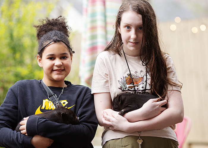 Two girls holding small black puppies outside, with colorful striped curtains in the background.