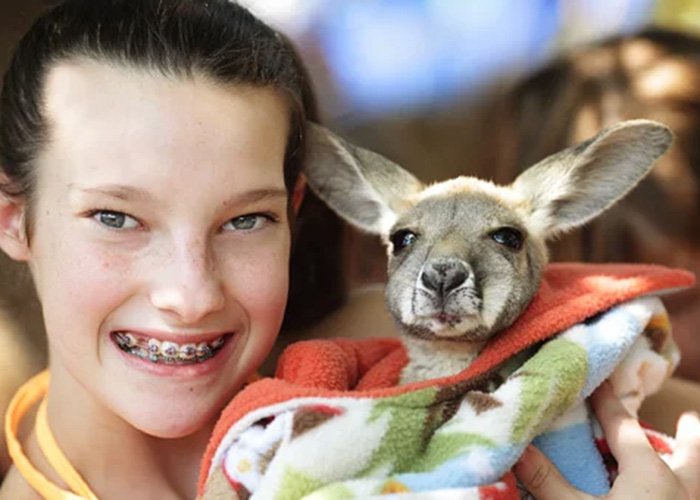 A smiling girl with braces holding a small dog wrapped in a colorful blanket in her arms.