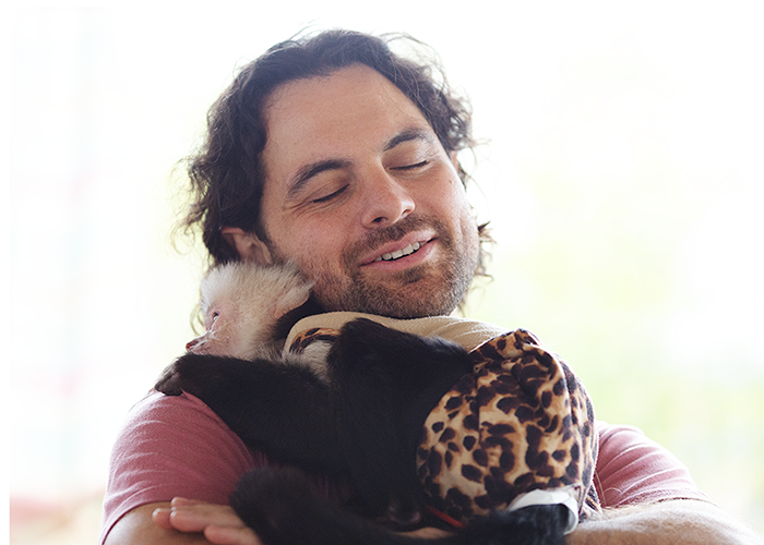 Man hugging a monkey dressed in a leopard-print outfit with a bow