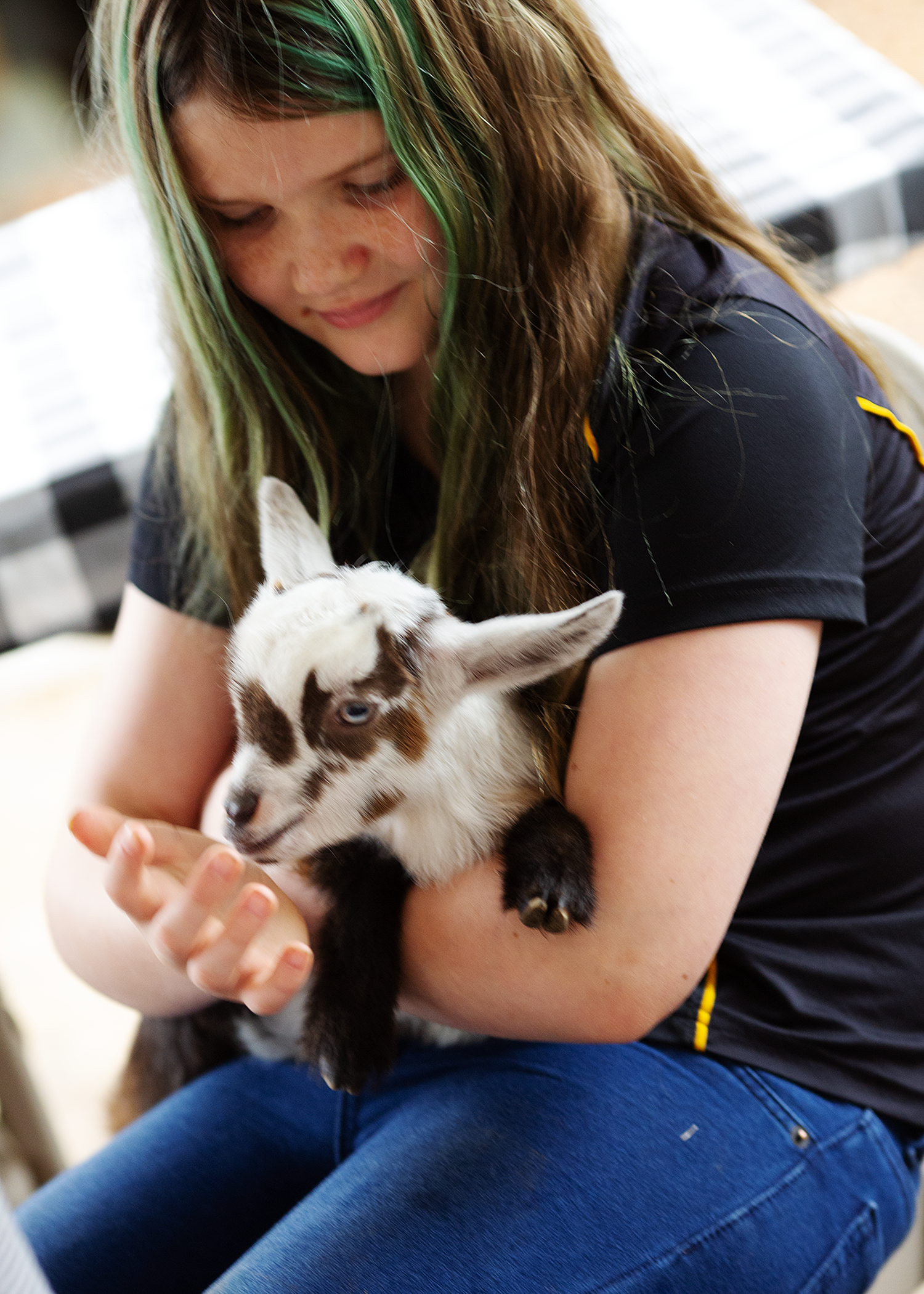 A girl with green and blonde hair holding a black and white kitten in her arms.