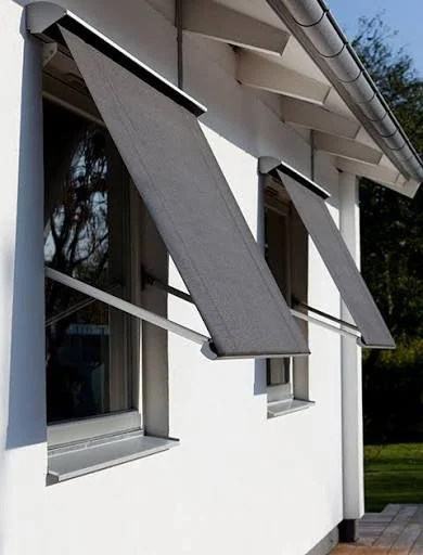 Twee opklapbare zonweringen die buiten aan een wit gebouw hangen.