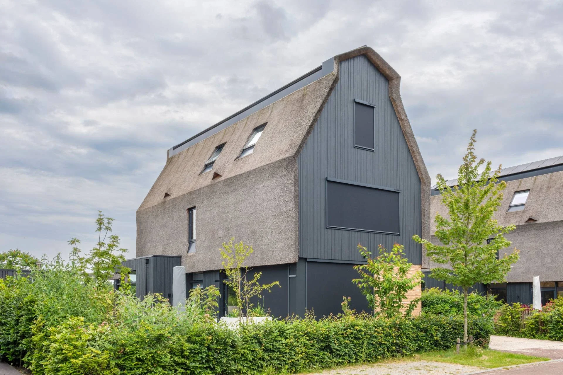 Modern huis met een combinatie van betonnen en houten gevels, een schuin dak met kleine ramen, omgeven door groen landschap en een pad voor het huis.