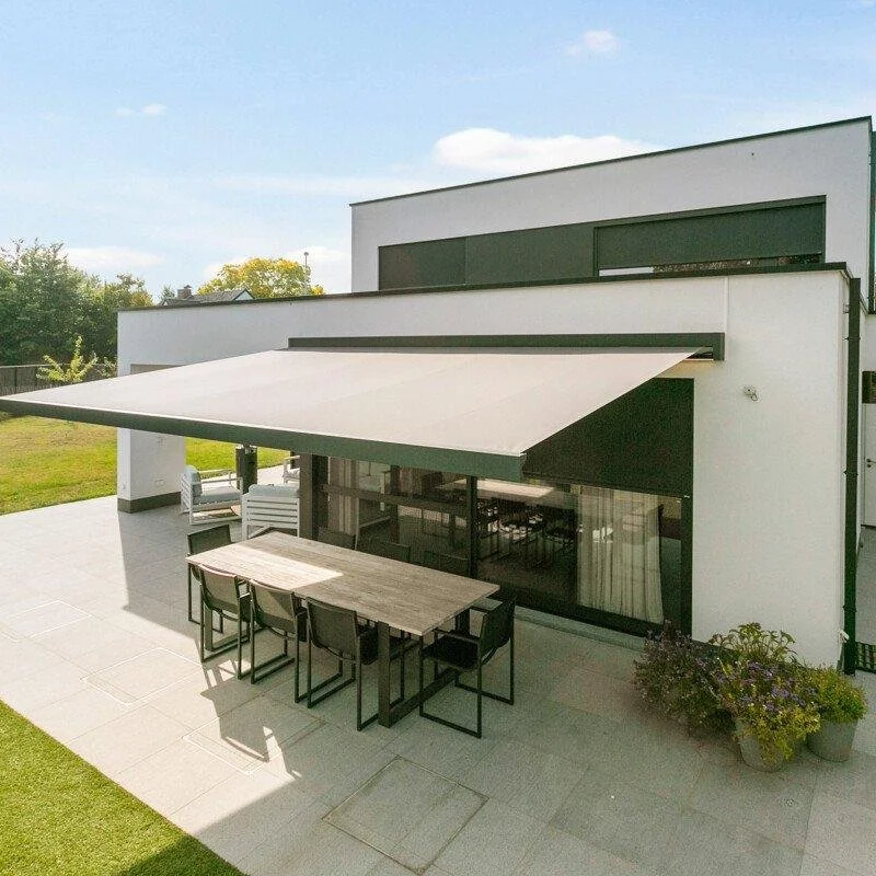 Moderne huis met een grote patio, een uitklapbare zonwering, een eettafel met zes stoelen, tuinstoelen en planten buiten.