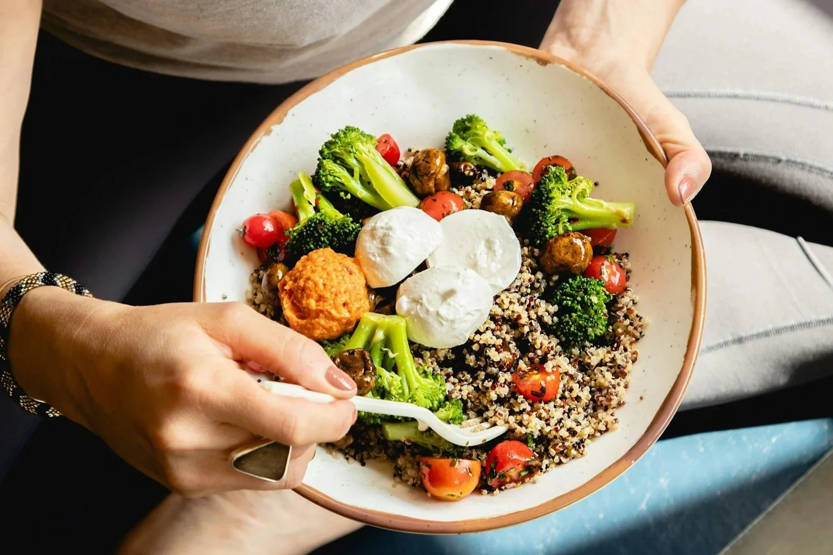 A person holding a bowl of quinoa, vegetables and eggs, illustrating a balanced meal.