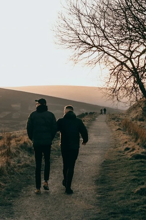 Two people walking together along a countryside path with rolling hills in the background.