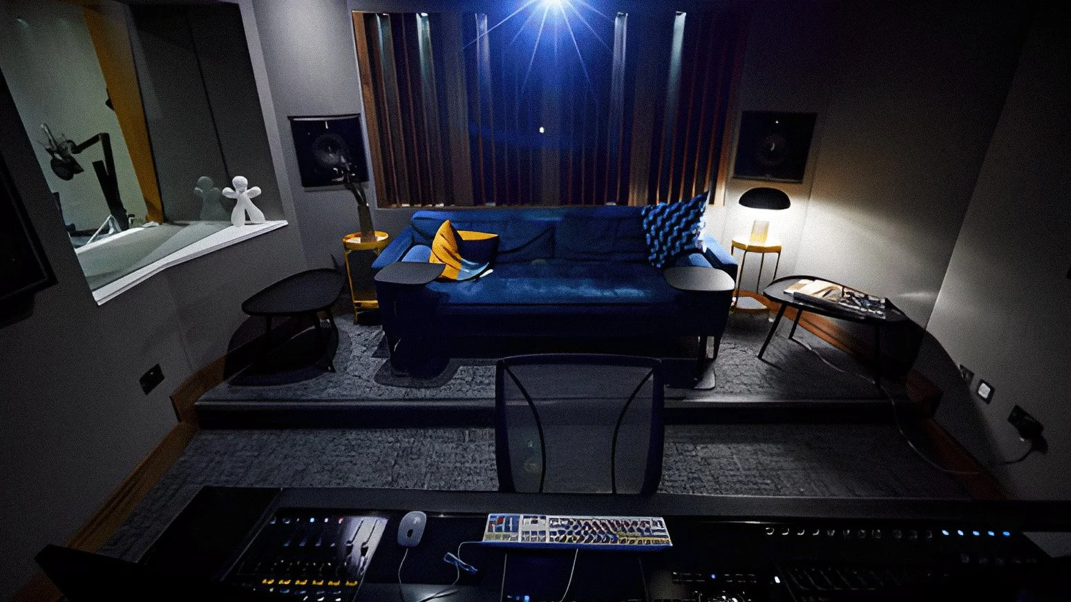 Recording studio with a blue velvet couch, yellow side tables, black and yellow pillows, soundproof walls, and recording equipment in the foreground.