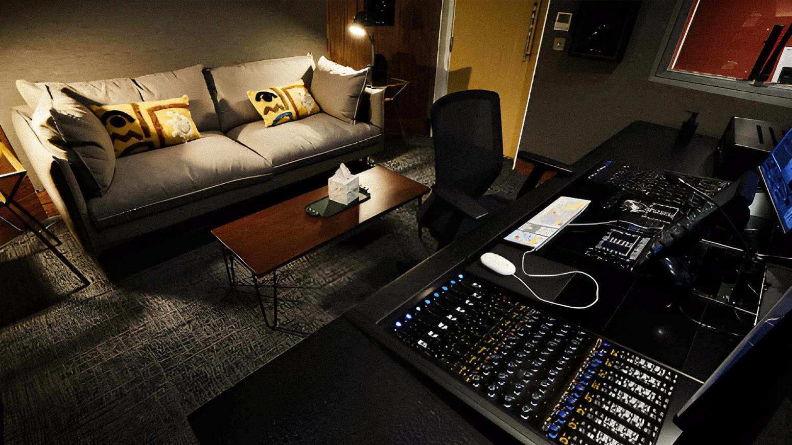 A recording studio with a sound mixing board, a computer monitor, and a black office chair, adjacent to a cozy living area with a gray sofa and decorative pillows, a wooden coffee table, and a floor lamp.