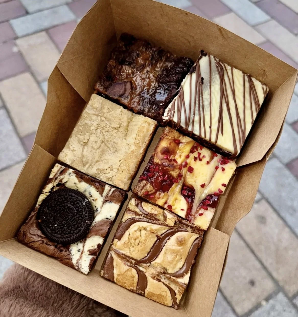A box of six assorted brownies and blondies, featuring, caramelised bannana brownie, triple chocolate with white chocolate ganache, raspberry cheesecake, nutella blondie, oreo brownie with cookies and cream.