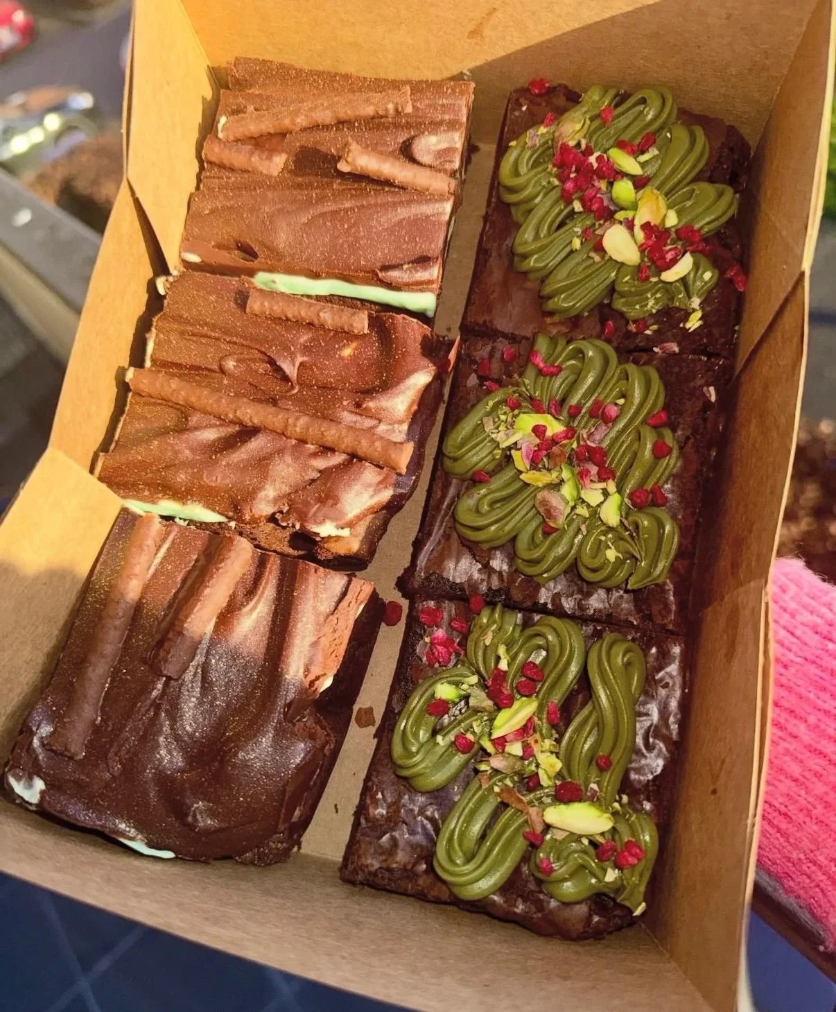 A box of six assorted brownies and blondies, featuring, pistachio brownie with pistachio cream and freeze dried raspberries and mint brownie with peppermint filling and mint ganache.