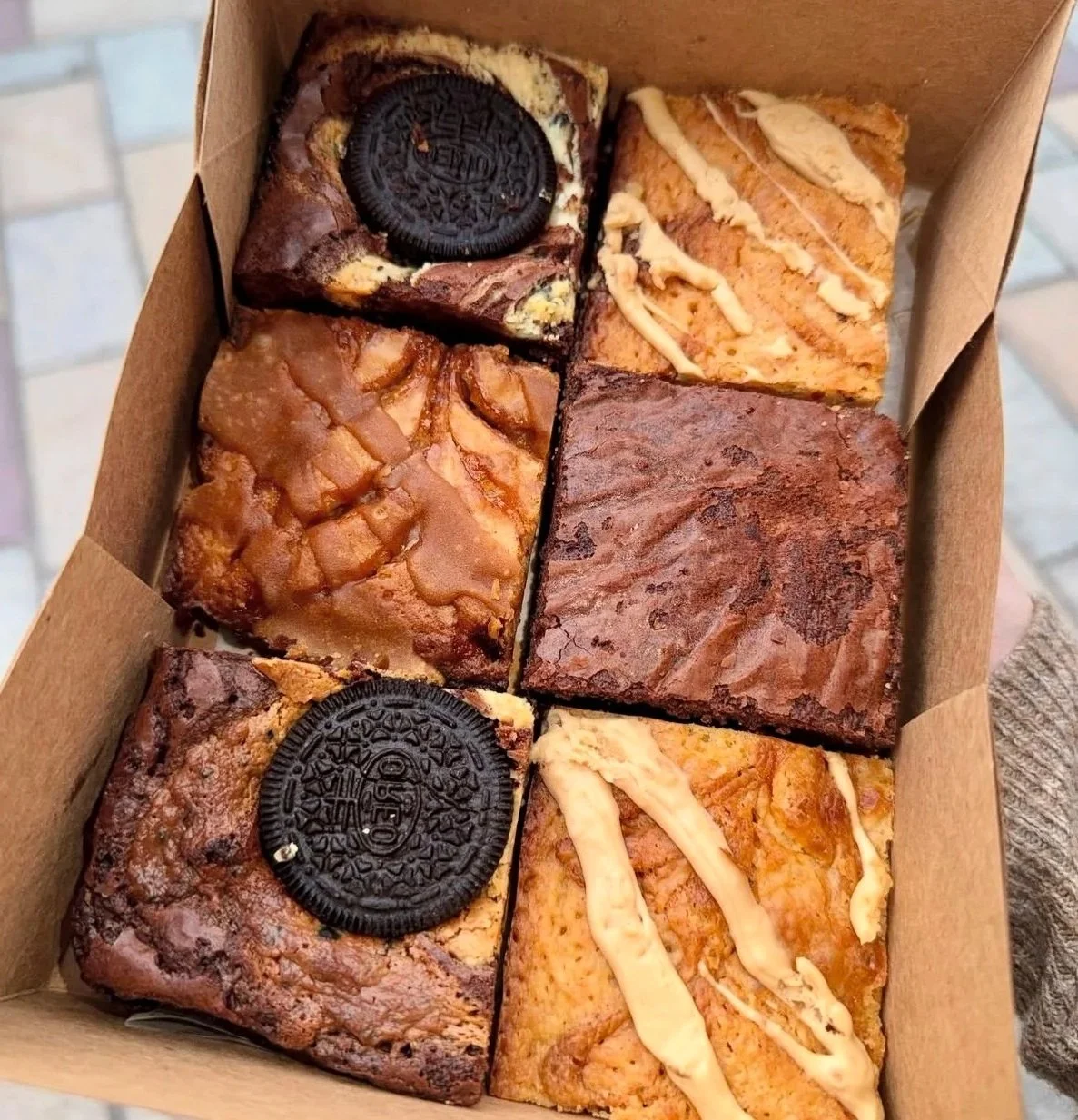 A box of six assorted brownies and blondies, featuring, oreo brownie with cookies and cream swirl, brookie brownie and golden blondie.
