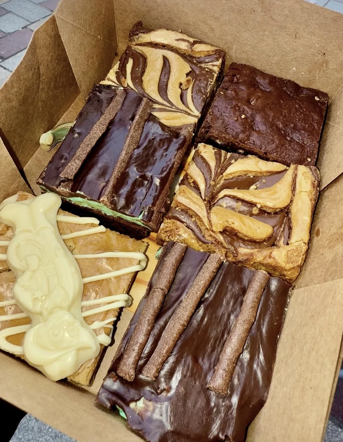 A box of six assorted brownies and blondies, featuring, mint brownie with peppermint filling and mint ganache, Milybar blondie, nutella blondie and triple chocolate brownie.