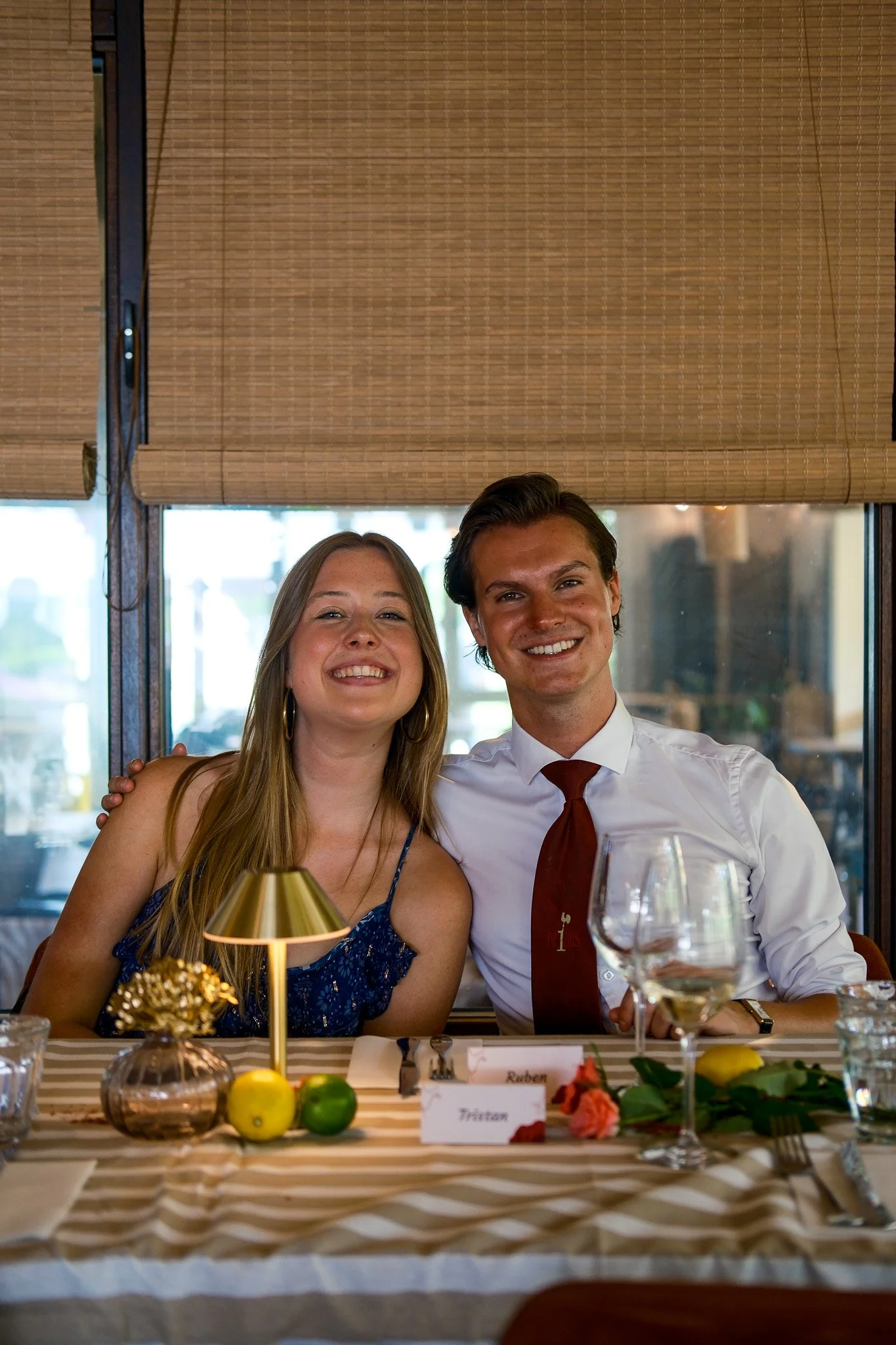 Twee mensen zitten aan een gedekte tafel tijdens een feestelijk diner, glimlachend naar de camera.