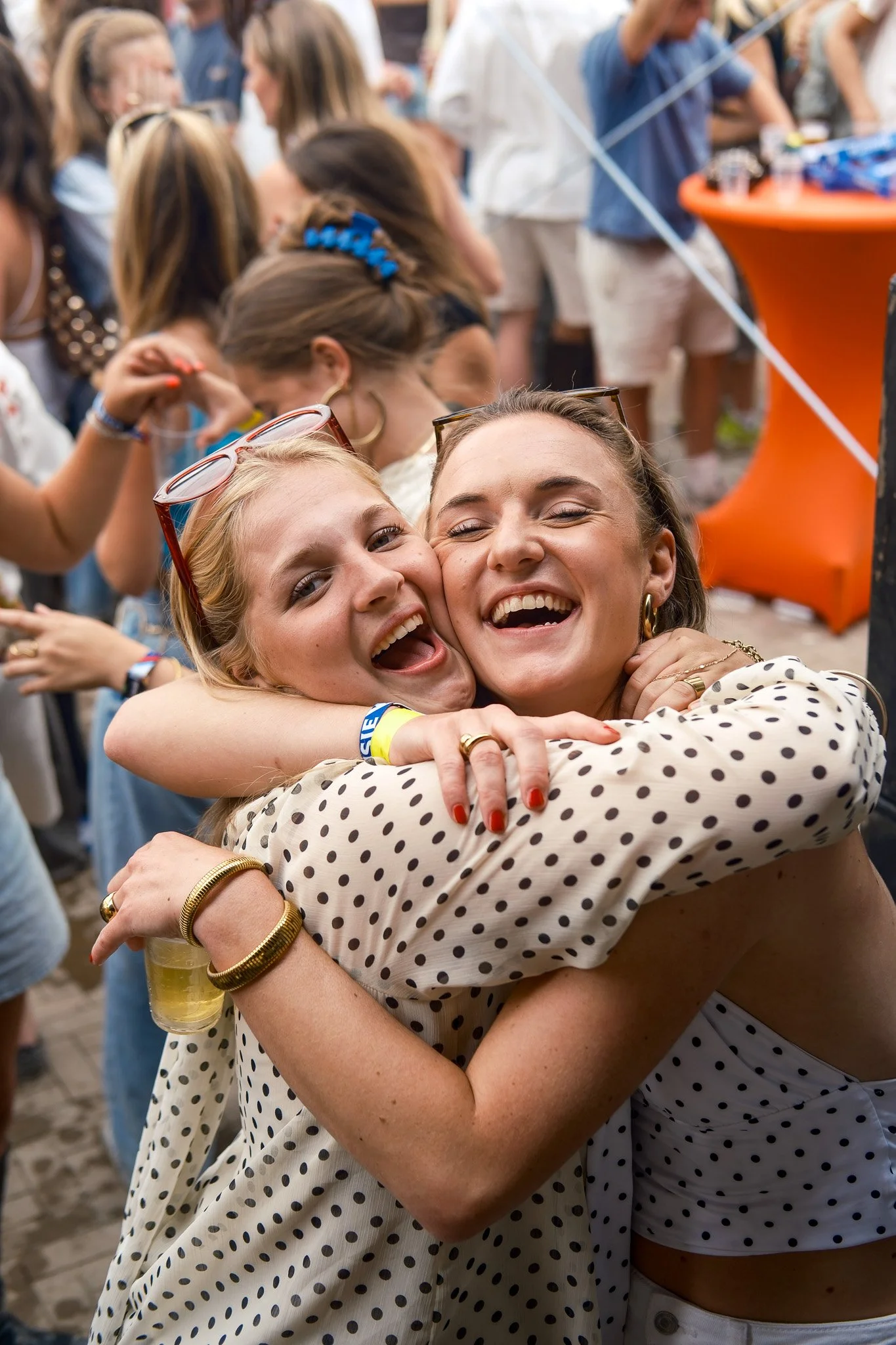 Twee vrouwen die elkaar omhelzen en lachen op een plein tijdens een druk feest of evenement.