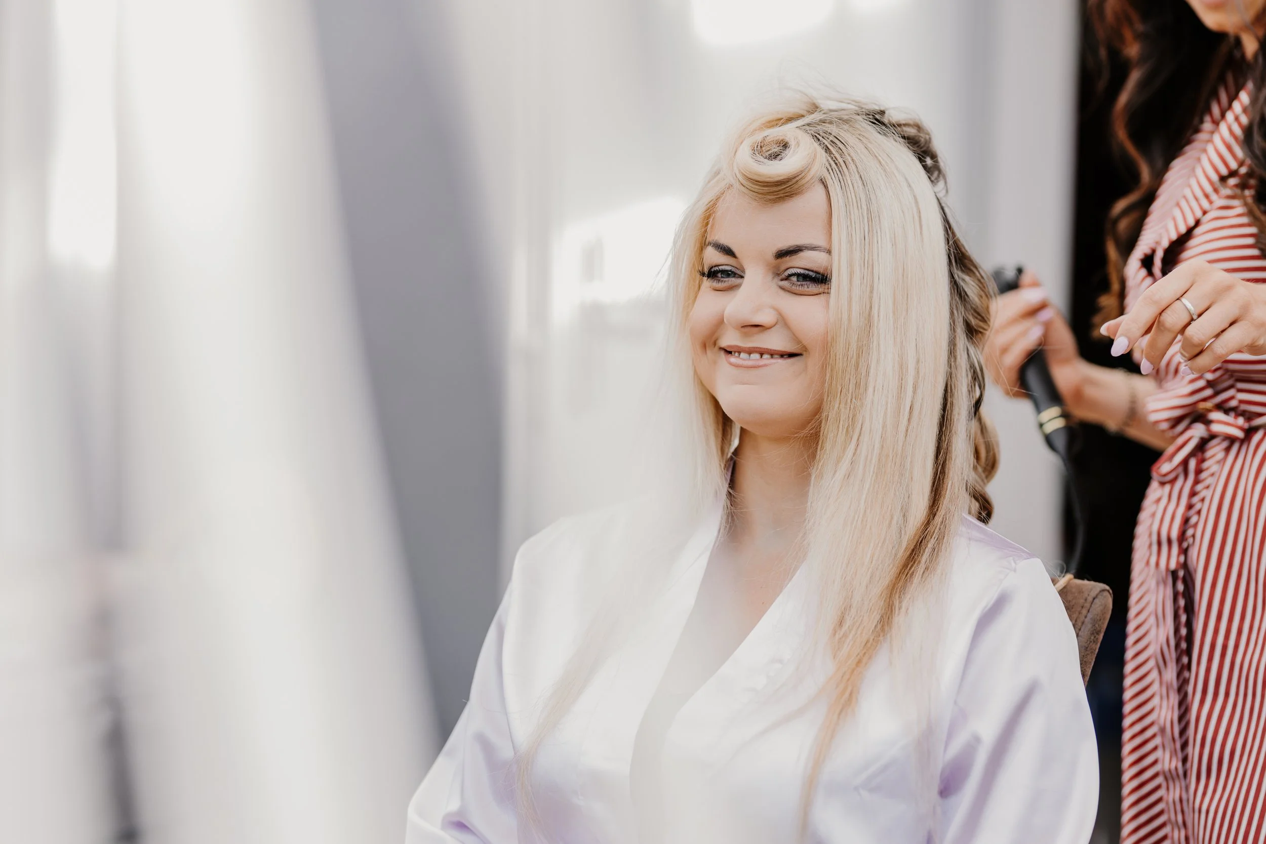 A woman with blonde hair getting her hair styled with rollers by a hairstylist.