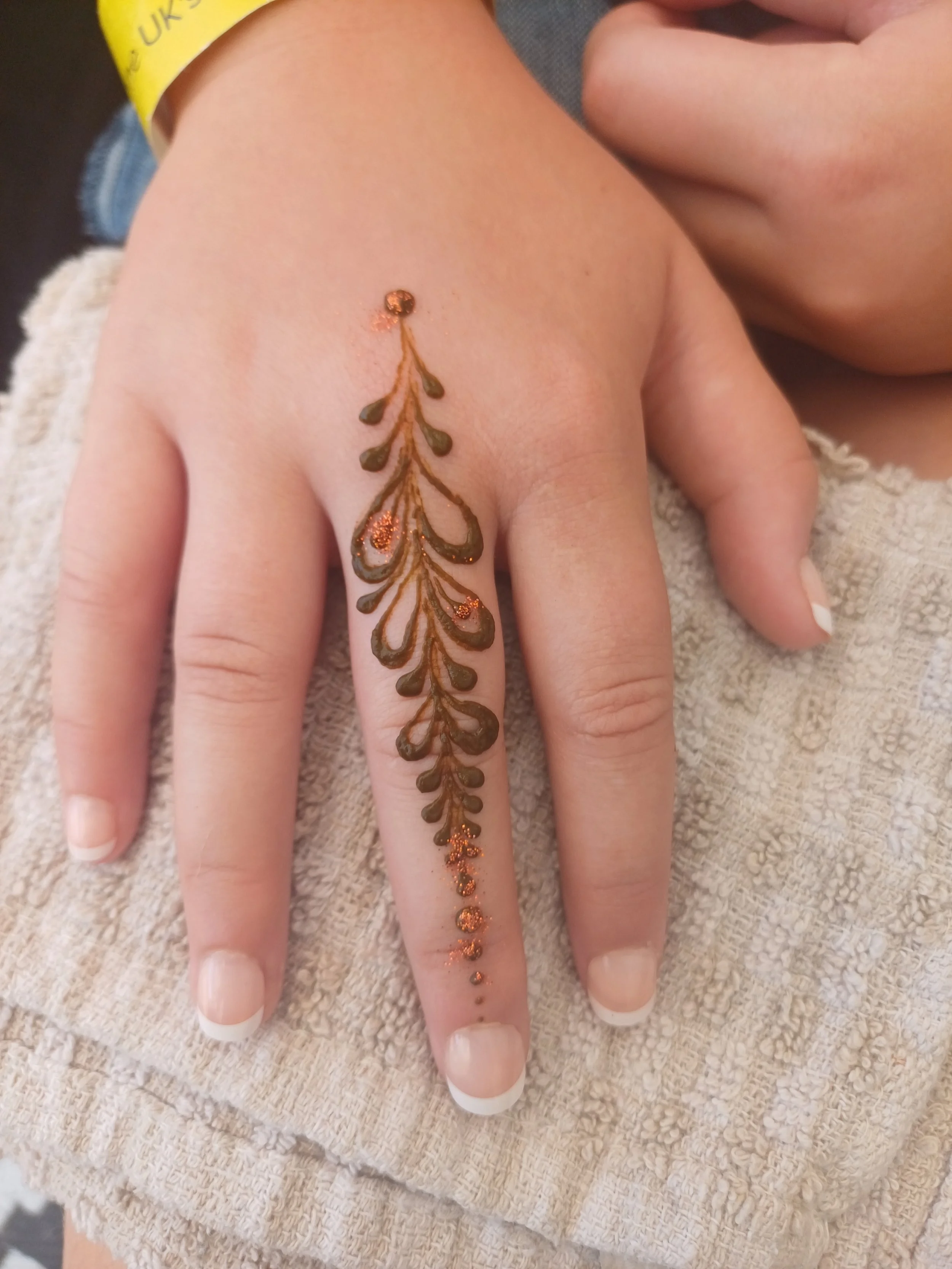Close-up of a woman's hand with a henna tattoo on her middle finger, resting on a textured, beige fabric surface.
