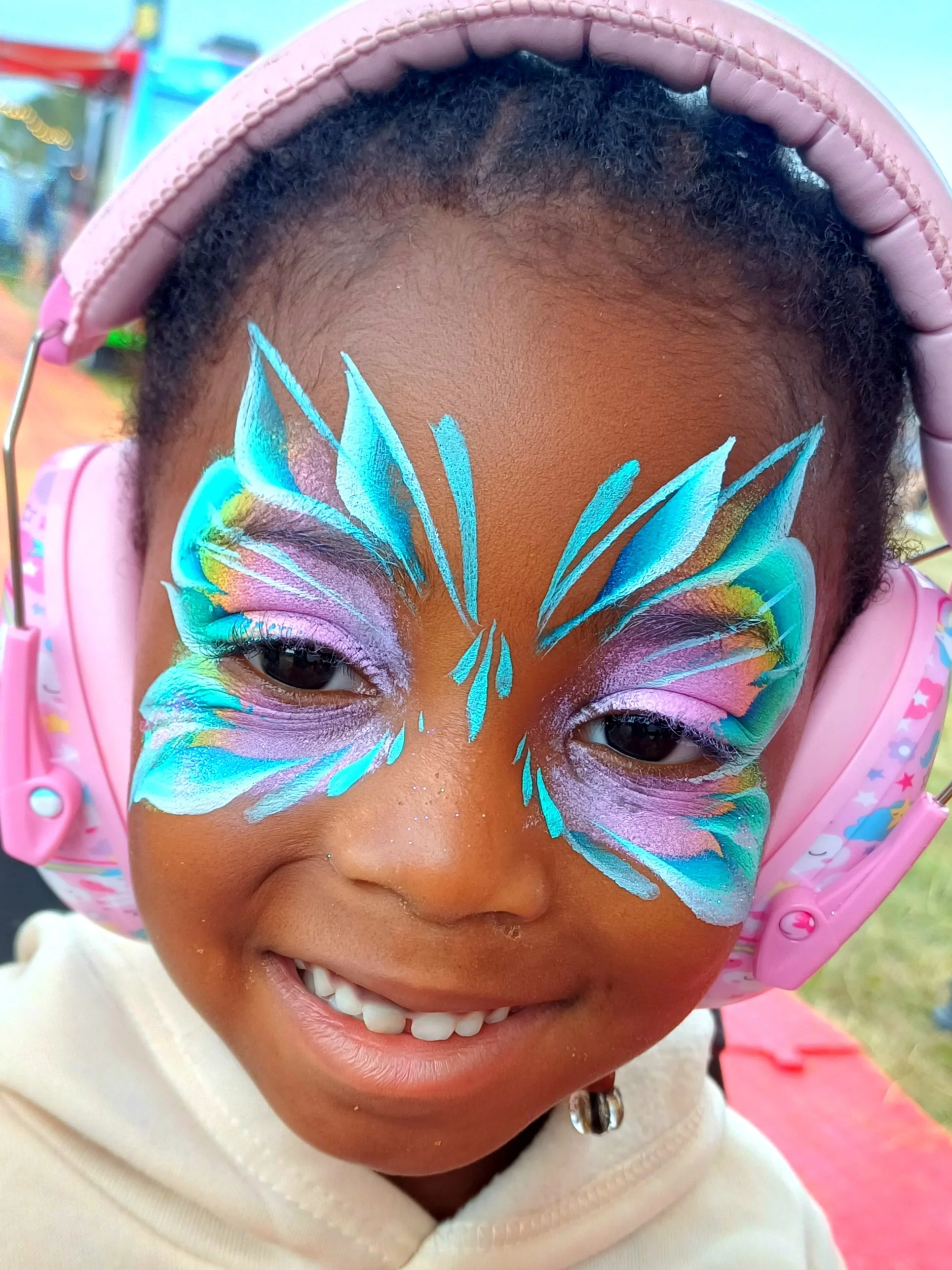 Close-up of a young girl wearing a pink headset with her face painted as a colorful butterfly design.