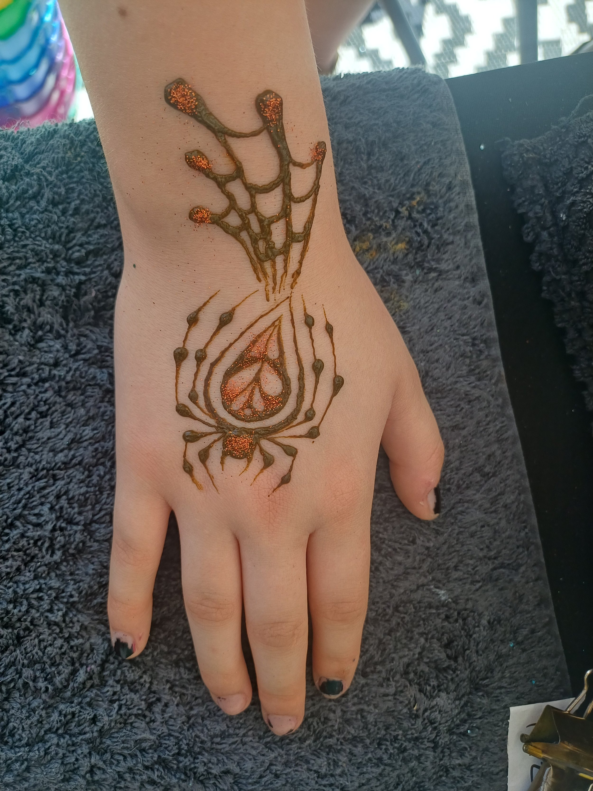 A tattoo of a scorpion on a person's hand and wrist, decorated with orange glitter.