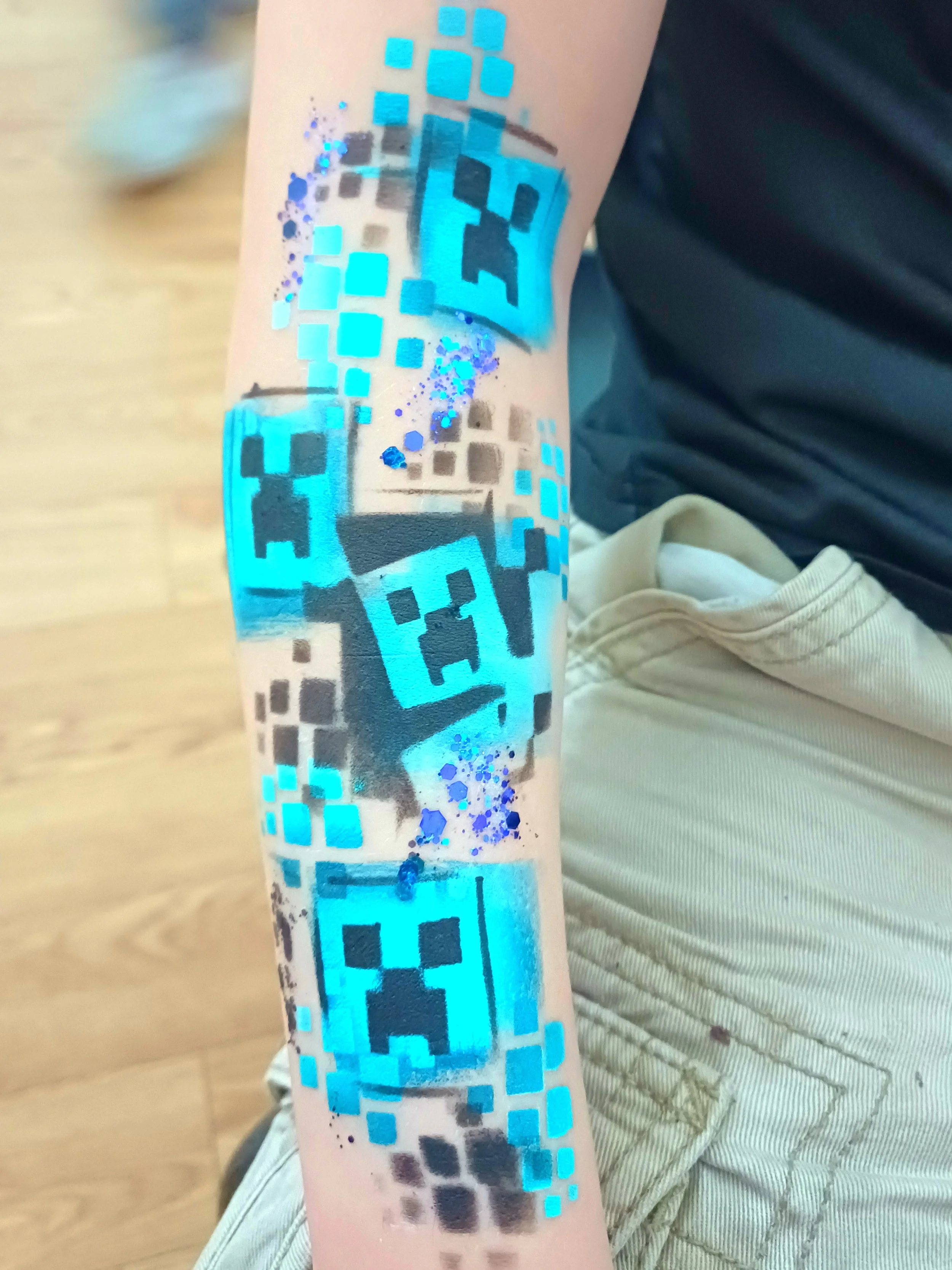 Temporary tattoo style body paint with pixelated blue and black Minecraft design on a person's forearm.