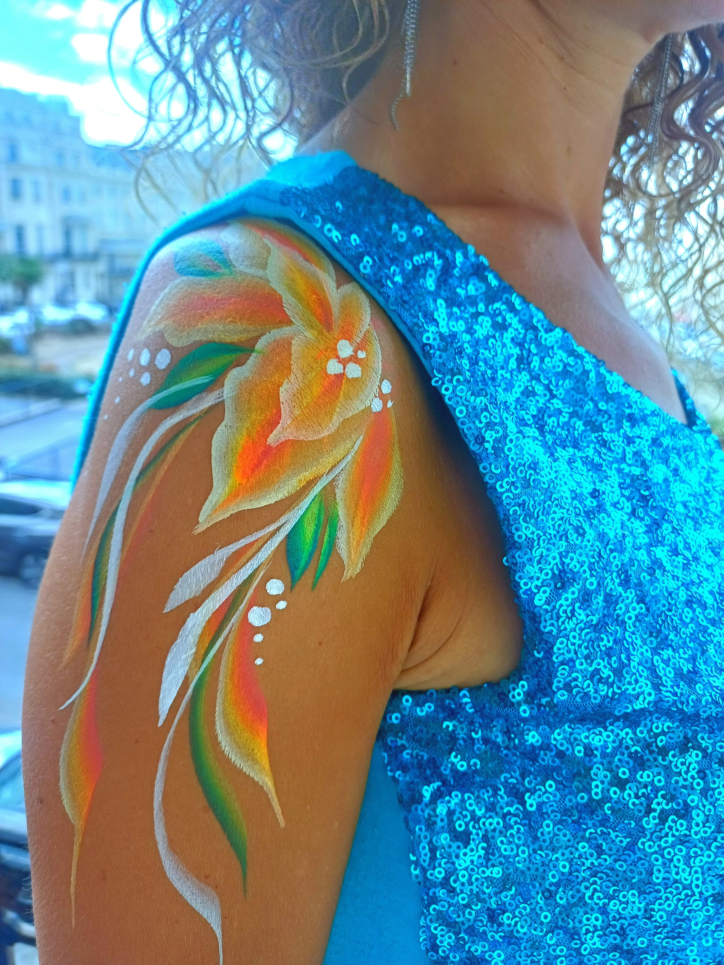 A person's shoulder with a brightly-colored floral tattoo and a shimmering blue sequin dress or top.