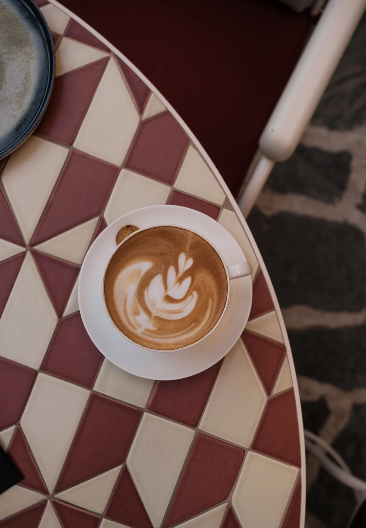 Latte in a white cup on a red and cream tiled café table.