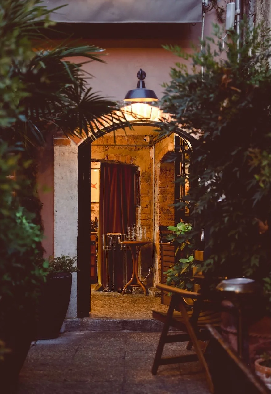 Warmly lit café entrance surrounded by greenery.