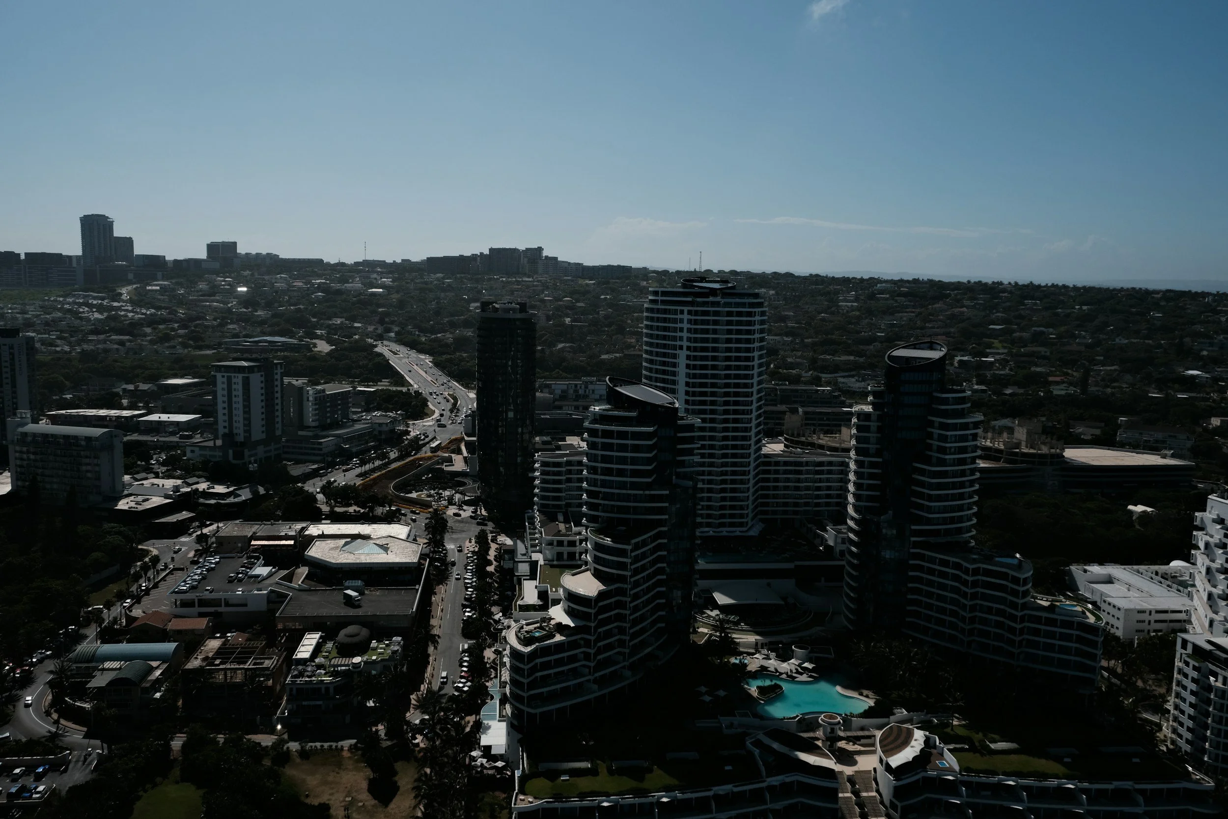 A city skyline with tall buildings, a highway, and residential area under a blue sky.