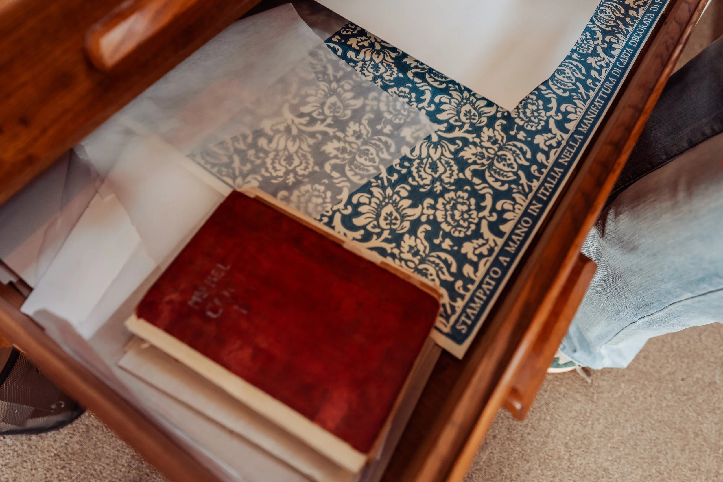 Open wooden drawer containing decorative paper and a beige envelope.